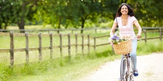 Lachende vrouw op de fiets met bloemen in de fietsmand