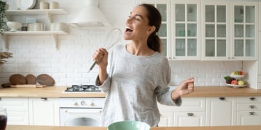 Vrouw bakt en zingt in de keuken met garde in de hand