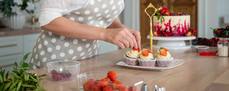 Vrouw in keuken versiert cupcakes met aardbeien